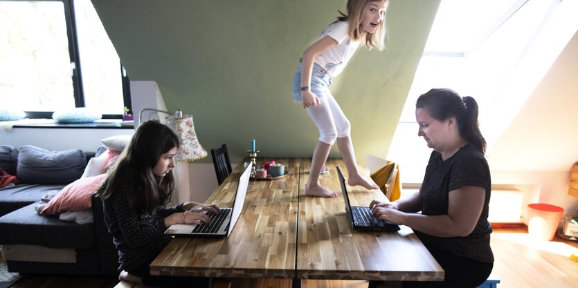 Mädchen läuft über den Tisch, Mutter und Schwester arbeiten