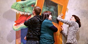 Drei Menschen versuchen eine Tür zuzudrücken, durch die ein Dinosaurier eindringen will