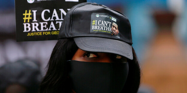 Eine Frau mit Mundschutz und Cap mit der Aufschrift "I can't breathe".