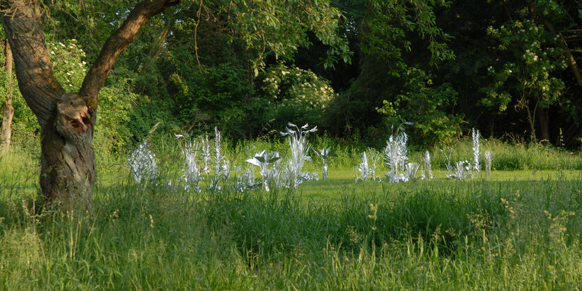 Neben einem Baum ragen aus dem Gras Blätter aus Aluminium.