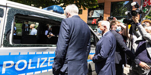 Horst Seehofer steht mit dem Rücken zur Kamera vor einer Polizeiwanne mit zerstörten Fensterscheiben