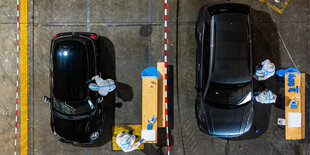 Von oben fotografierte Autos. Menschen in weißen Anzügen sprechen mit den Fahrern oder Fahrerinnen