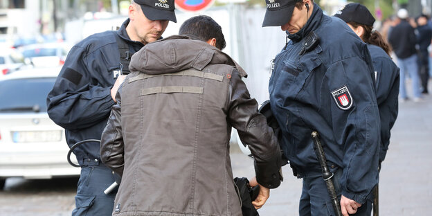 Zwei Polizisten kontrollieren den Rucksack eines Mannes