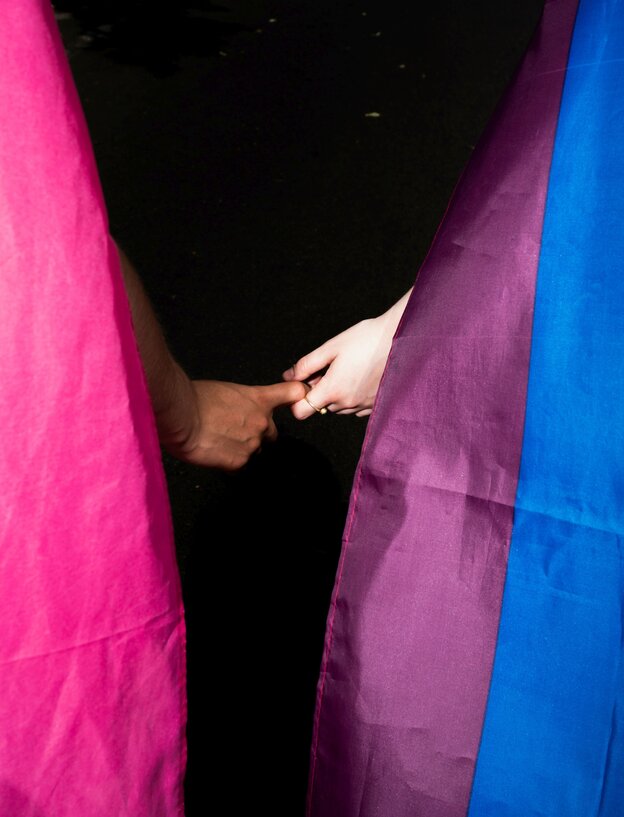 Zwei Regenbogenfahnen und Händer zweier Menschen, die sich berühren Zwei Regenbogenfahnen und Händer zweier Menschen, die sich berühren
