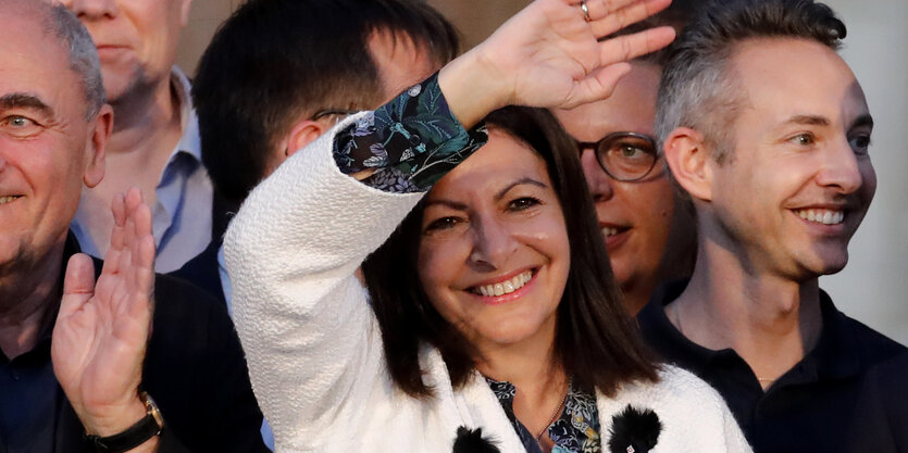 Umringt von anderen winkt Anne Hidalgo in Richtung des Fotografen