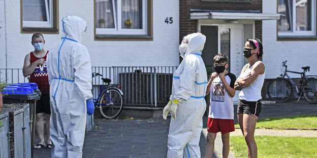 Menschen, manche sommerlich gekleidet, manche in Schutzanzügen Menschen, manche sommerlich gekleidet, manche in Schutzanzügen