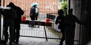 Polizisten stehen vor einem Bauzaun, Bewohner dahinter