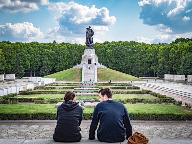 Zwei junge Leute sitzen auf Steinen und schauen auf das Sowjetische Ehrenmal im Treptower Park