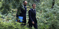 President Emmanuel Macron und Ministerpräsident Edouard Philippe laufen durch einen Busch.