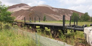 Flachbett-Eisenbahnwaggons, dahinter ein braun-grauer Schuttberg