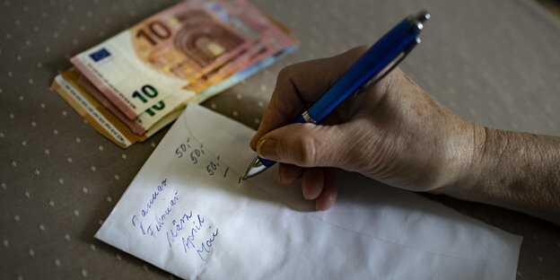Eine ältere Person schreibt Monatsausgabe auf einen Zettel.