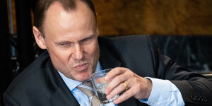 Ein Mann mit großen Geheimratsecken macht ein verkniffenes Gesicht und trinkt ein Glas Wasser
