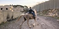 Ein Junge reitet auf einem Pferd an einer Mauer entlang