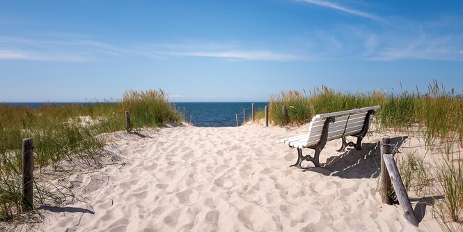 Sand, Meer, Strandgras und eine weiße Parkbank