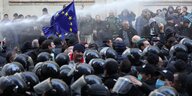 Demonstration mit EU-Fahne vor Polizisten mit Helmen.