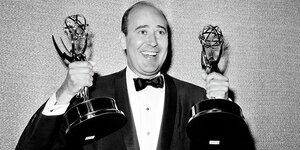 Ein Mann im Smoking hält zwei Emmy-Statuen in den Händen.
