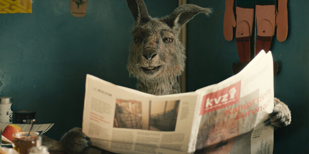 Ein Känguru sitzt am Küchentisch mit einer aufgeschlagenen Zeitung