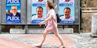Eine Frau läuft durch eine Straße und im HIntergrund sind Wahlplakate für Louis Aliot aufgestellt