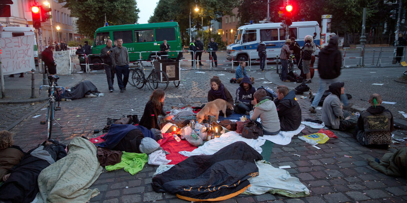 Menschen sitzen auf der Straße, dahiner die Polizei