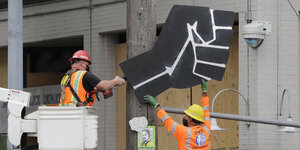 Zwei Arbeiter demontieren eine große Abbildung einer schwarzen Faust.
