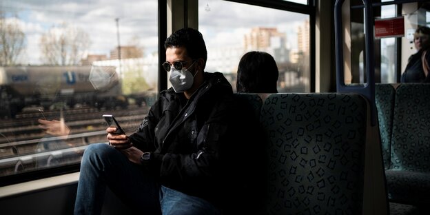 Ein Mann mit Handy und Schutzmaske in der Bahn