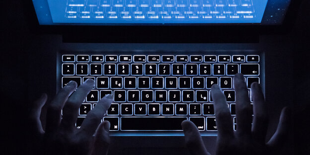 Jemand tippt im Dunkeln auf einem Laptop dessen Bildschirm blau strahlt