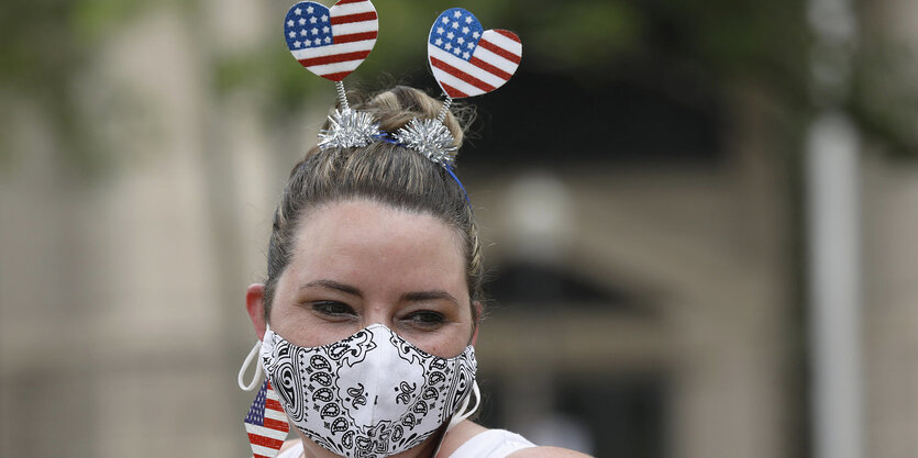 Eine Frau trägt eine Mundschutzmaske und amerikanische Fähnchen als Haarschmuck