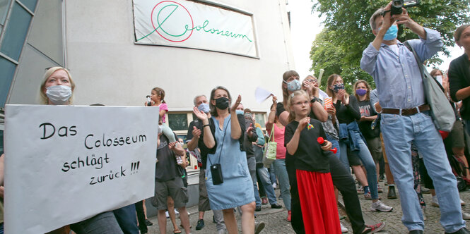 Menschen stehen mit Schildern vor einem Kino