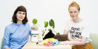 Zwei junge Frauen, Luise Zaluski und Julia Seeliger, sitzen an einem Tisch. Auf dem Tisch stehen Reinigungsutensilien.