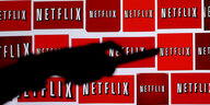Der Schatten einer Hand mit Fernbedienung, im Hintergrund einige Netflix-Logos.