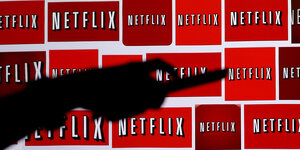 Der Schatten einer Hand mit Fernbedienung, im Hintergrund einige Netflix-Logos.
