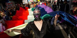 Eine Frau mit einer Sturmmaske hält eine Regenbogenfahne