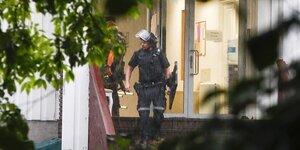 Ein Polizist steht im Eingang einer Moschee. Er trägt einen Schild und einen Helm, dessen Visier nach oben gepklappt ist.