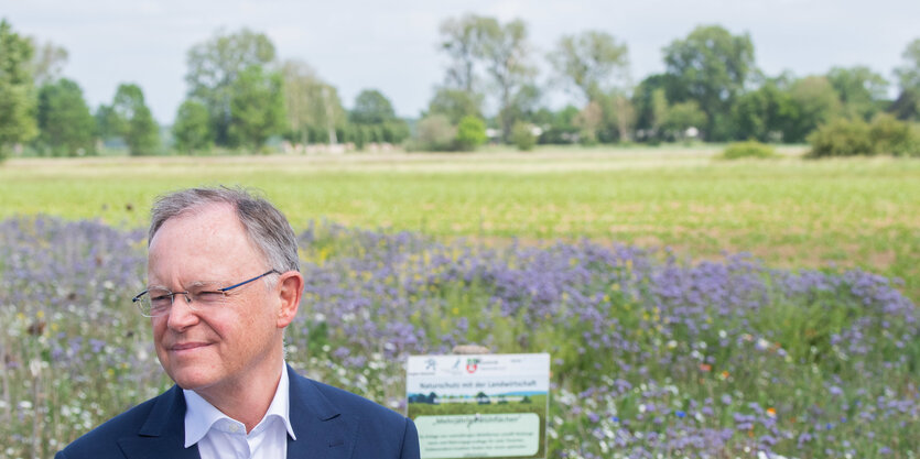 Ein Mann mit Brille vor einer blühenden Wiese, vor dem Horizon Bäume