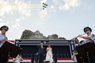 Das Ehepaar Trump auf einer Bühne unterhalb des Mount Rushmore. Am rechten und linken Bildrand stehen Militärorchestermusiker