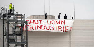„Shut Down Tierindustrie"-Transparent hängt an der Fassade eines Gebäudes. Auf dem Dach befinden sich mehrere Menschen