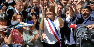 Michèle Rubirola steht in einer Menschenmenge und klatscht in die Hände. Sie trägt die Scherpe des Bürgermeisterinnenamtes. Um Sie ist dichtes Gedränge, weil alle sie interviewen oder fotografieren wollen.