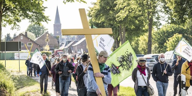 Menschen tragen ein Kreuz und Fahnen durch den Ort Keyenberg