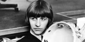 Ringo Starr als junger Mann 1965. Er hat dunkle Haare, die sein Gesicht umfassen. Er hält ein Tambourin in der Hand.