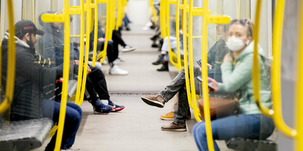 Fahrgäste sitzen in einer U-Bahn, wobei eine Frau einen Mundschutz trägt