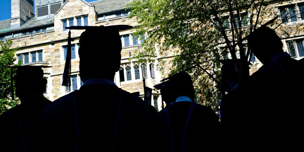 Studierende in vor ihrem Unigebäude, von hinten fotografiert. Sie tragen Dokturhut und Talar.