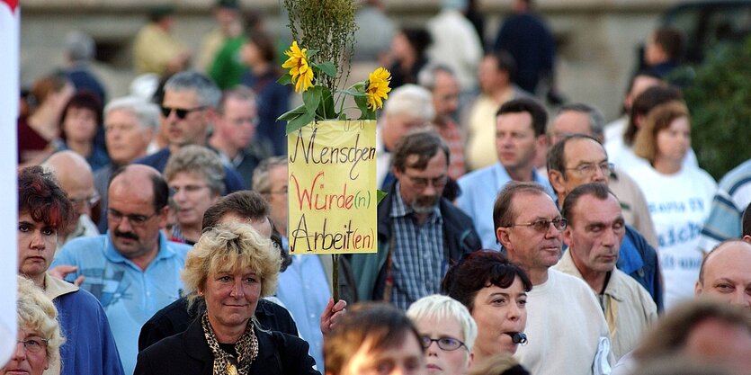 eine Menschenmenge, eine Frau trägt ein Transparent mit der Aufschrift"Menschen würden arbeiten"