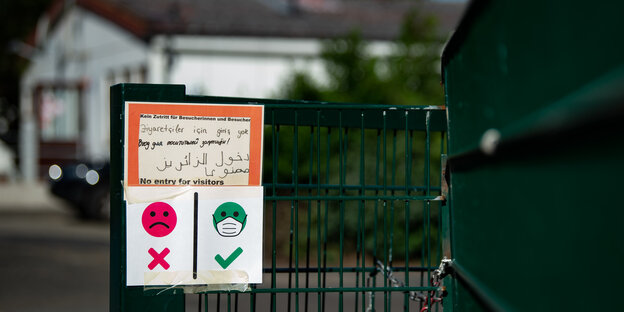 Ein Hinweisschild "Kein Zutritt für Besucherinnen und Besucher" und ein Plakat zum Tragen von Mund-Nasen-Maske ist am Eingang zum Grenzdurchgangslager Friedland vor einer Unterkunft zu sehen.