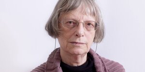 Potrait der Autorin Elke Erb, eine alte Frau mit grauen Haaren, die bis zur Wange reichen. Sie trägt eine Brille mit Brillenband um den Nacken.
