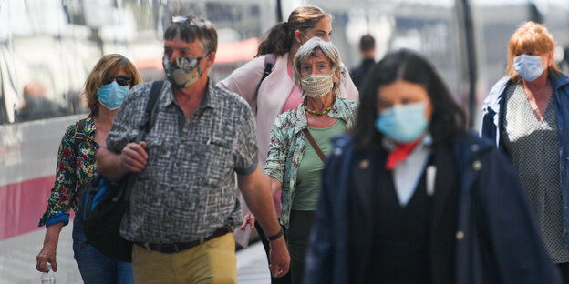 Menschen sind auf einem Bahnsteig und tragen Mundschutzmasken