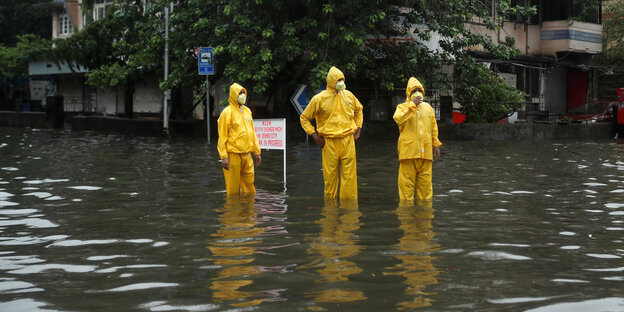 Städtische Mitarbeiter mit Mund-Nasen-Schutzmaske stehen in einer überfluteten Straße