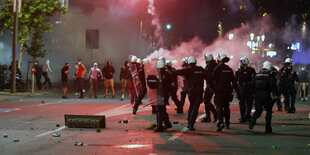 Eine Gruppe Polizisten steht vor Demonstrierenden, die Bengalos halten. Es ist später Abend.