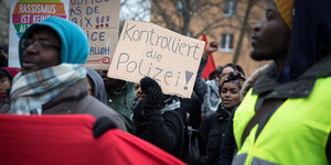 Eine Menschenmenge, ein Mann hält ein Schild mit der Aufschrift "Kontrolliert die Polizei"
