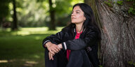Schauspielerin und Sängerin Jasmin Tabatabai sitzt im Schlosspark in Pankow an einen großen Baum geleht und schaut in den Himmel