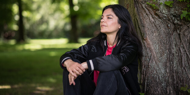 Schauspielerin und Sängerin Jasmin Tabatabai sitzt im Schlosspark in Pankow an einen großen Baum geleht und schaut in den Himmel